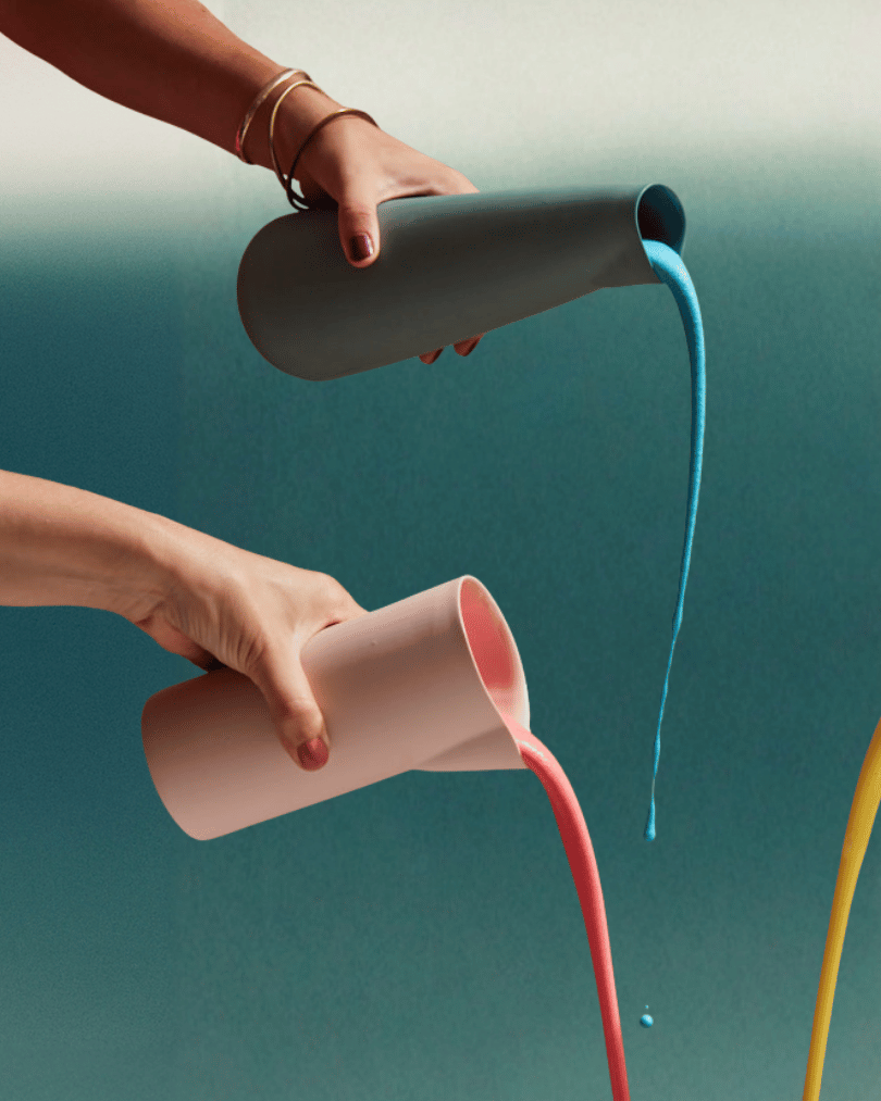 Two hands pouring colorful liquids from cylindrical containers against a gradient background