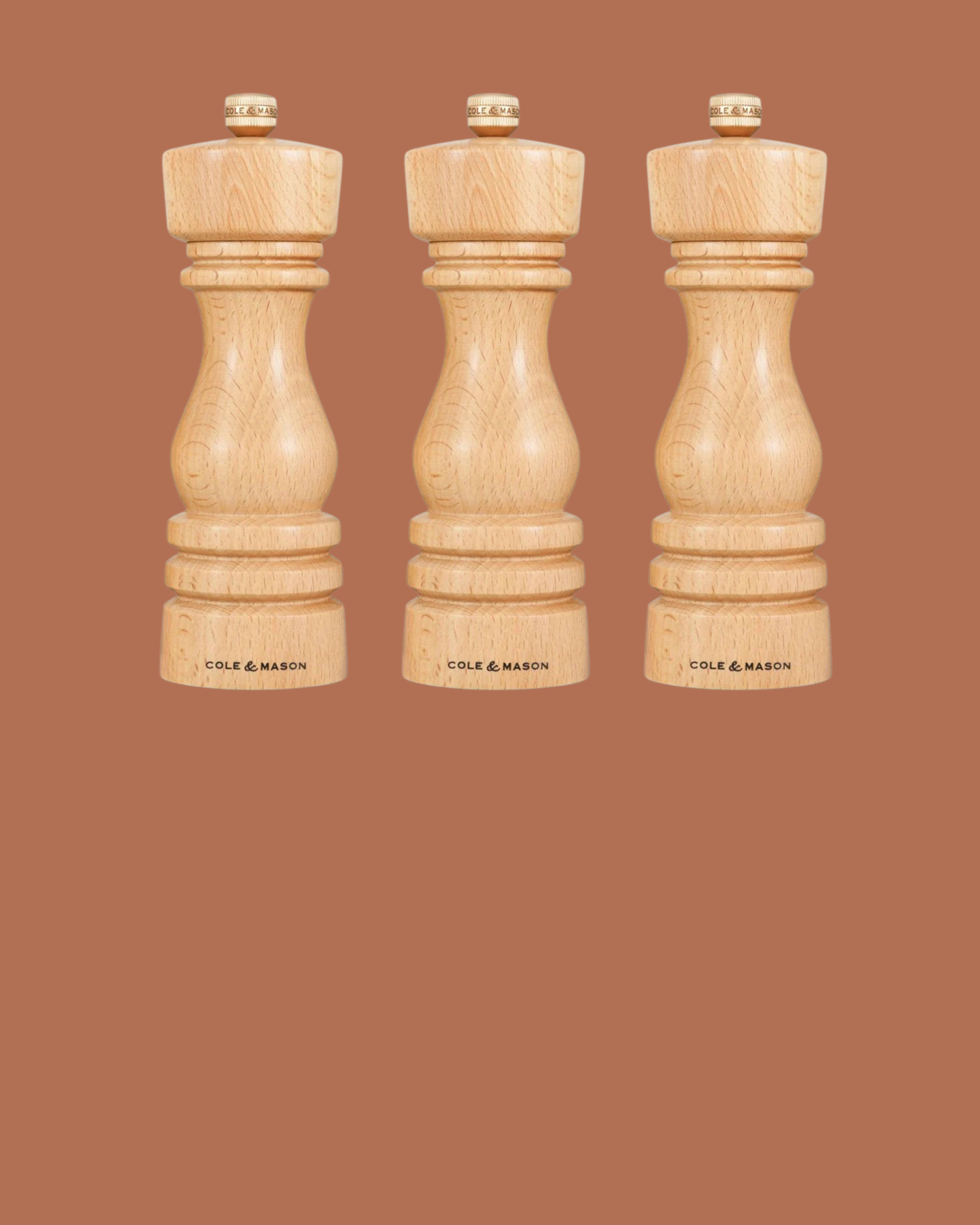 Three wooden pepper mills on a brown background